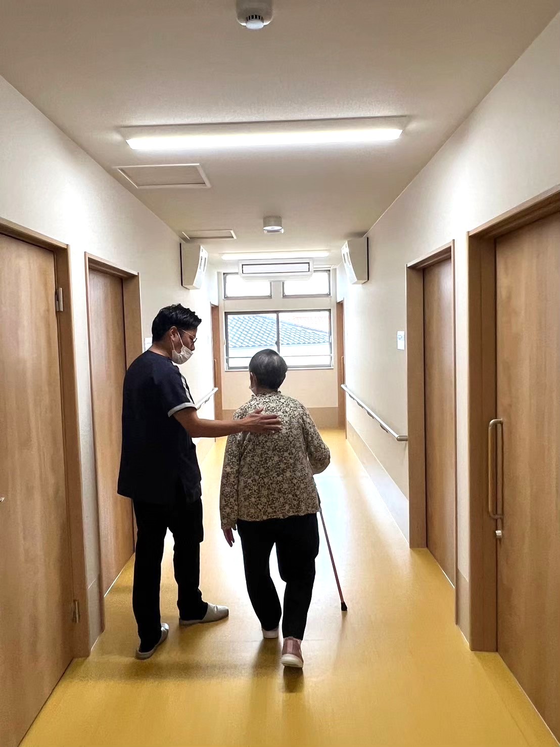 老人ホーム内で利用者さんの歩行リハビリを支えるスタッフ
